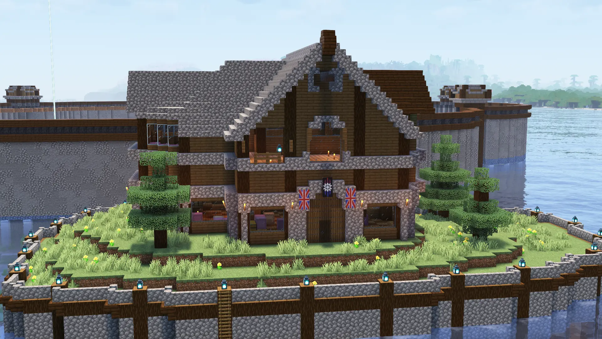 A three story spruce house with cobblestone accents and roof stands on an artificial island, with a few spruce trees placed around it. On the front door hands two banners, one with a white ring shape and another that depicts the flag of the United Kingdom.